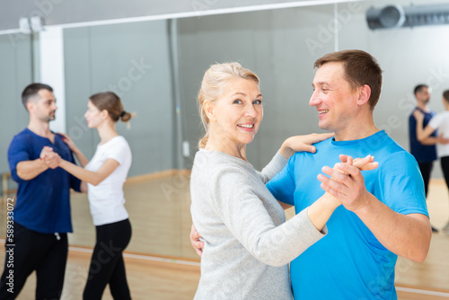 Middle-aged woman and man practicing bachata dance moves in pair during group class
