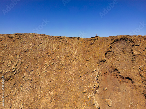 Dramatic image of a person standing on the ridge of the steep sided volcanic crater of Las Calderas volcano near Corralejo in Fuerteventura Spain