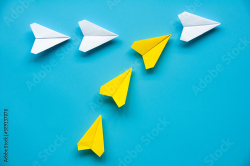 Yellow paper airplane origami joining other white airplanes on blue background with customizable space for text or ideas. Leadership concept.