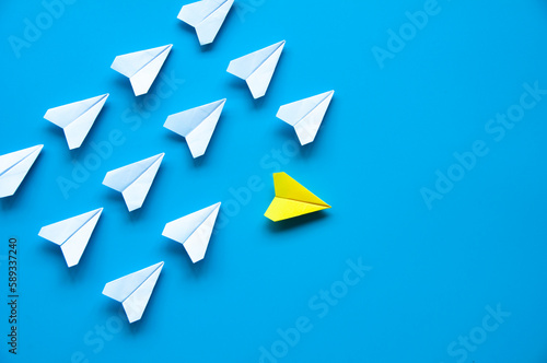 Yellow paper airplane origami leaving other white airplanes on blue background with customizable space for text or ideas. Leadership skills concept.