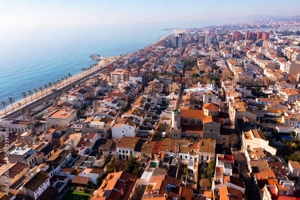 Scenic aerial view of coastal area of Spanish city of Vilassar de Mar overlooking brownish roofs of buildings and sandy seashore on sunny winter day, Catalonia