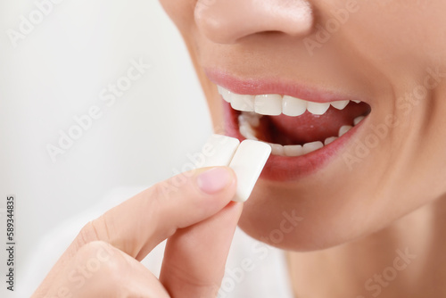 Woman putting chewing gum pieces into mouth on blurred background, closeup