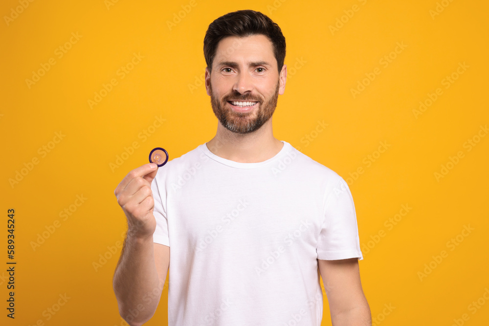 Happy man holding condom on yellow background. Safe sex Happy man holding condom on yellow background. Safe sex