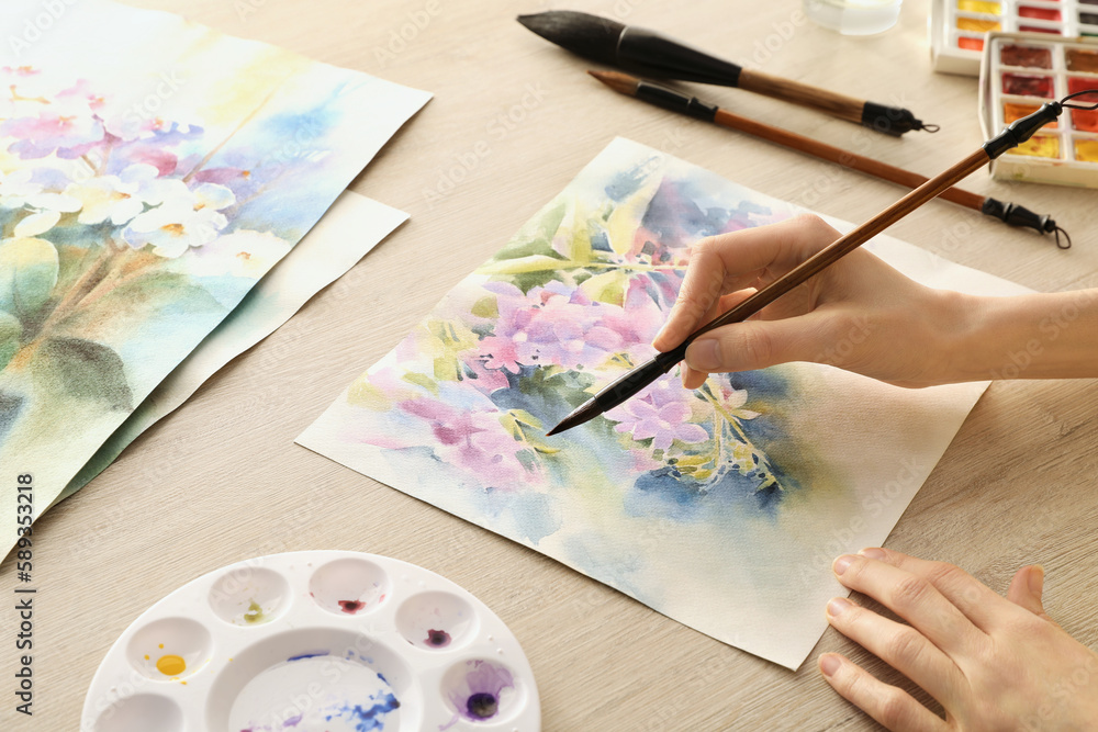 Woman painting flowers with watercolor at white wooden table, closeup. Creative artwork Woman painting flowers with watercolor at white wooden table, closeup. Creative artwork