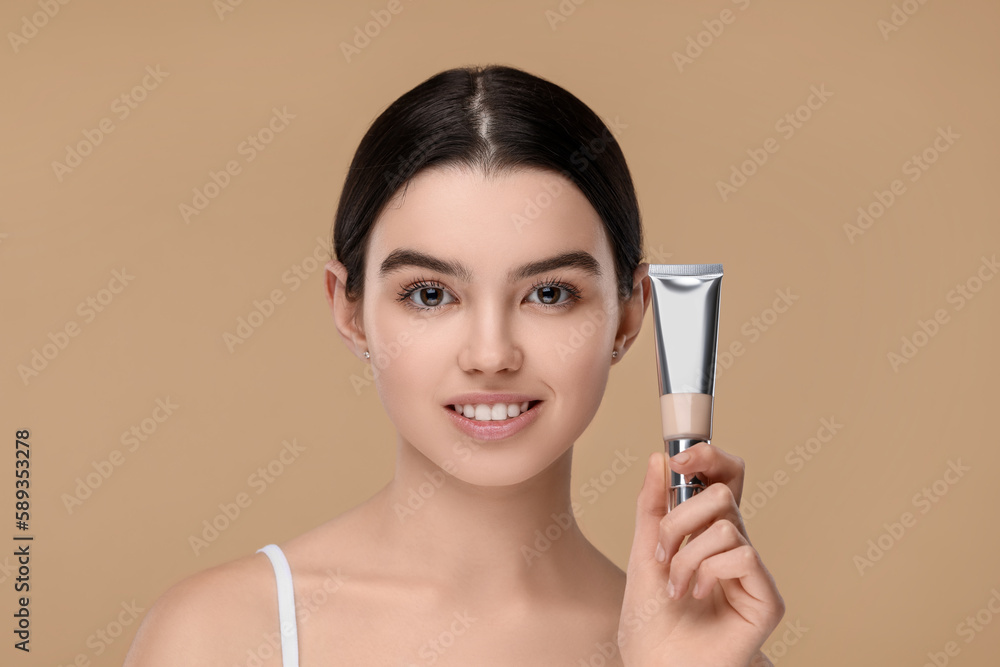 Teenage girl holding tube with foundation on beige background Teenage girl holding tube with foundation on beige background