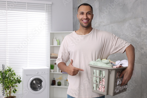 Happy man with basket full of laundry in bathroom. Space for text