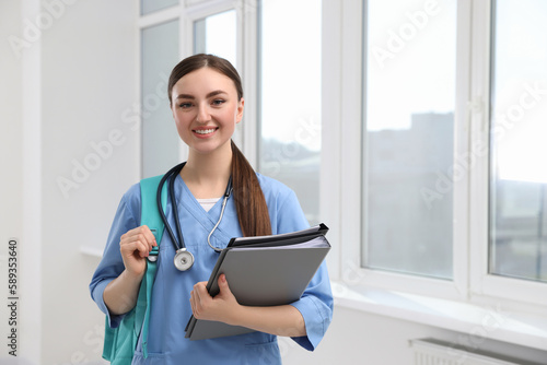 Smart medical student with folders in college hallway, space for text