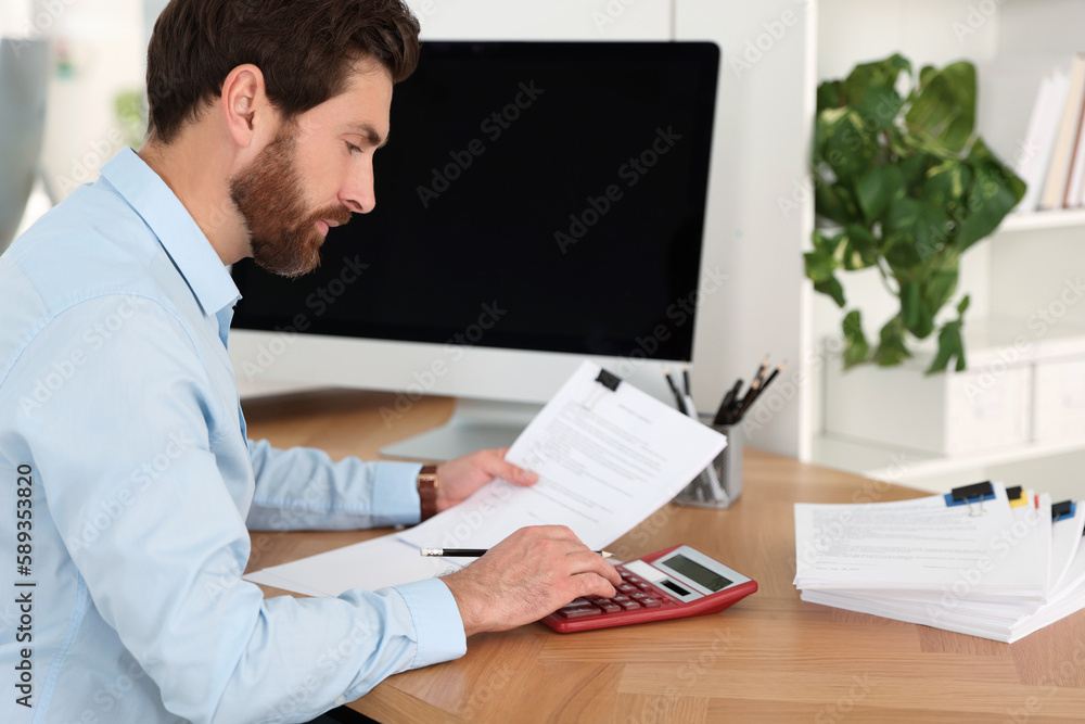 Man working with documents and using calculator at wooden table in office Man working with documents and using calculator at wooden table in office