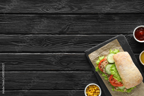 Food photography. Delicious sandwich with tuna, vegetables and sauces on black wooden table, flat lay with space for text