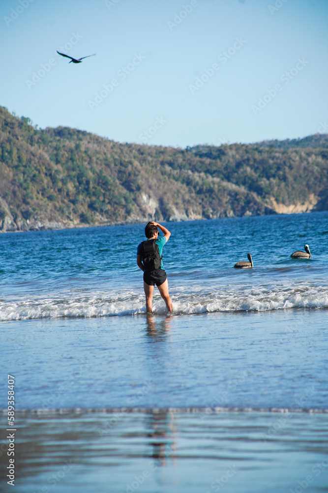 Joven con maleta caminando a la orilla del mar