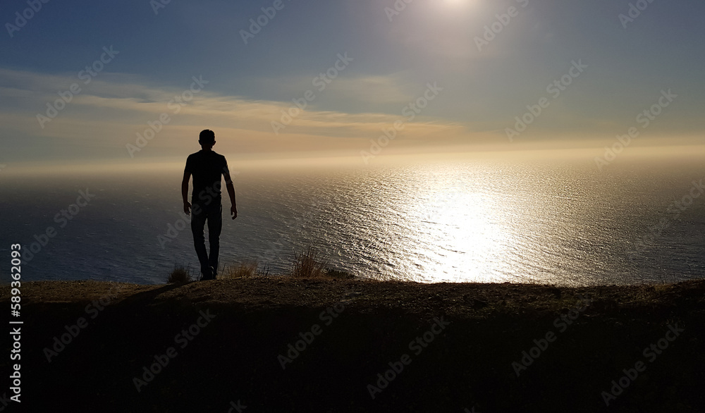 silhouette of a man walking towards the sunset along the calm sea or ocean background without waves