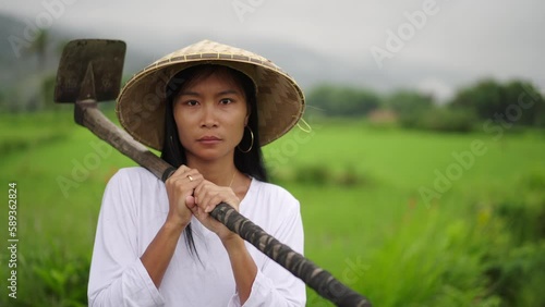 Serious young asian female rice farmer looking at camera holding farm equipment photo