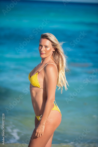 Young blonde woman in a yellow bikini running on the beach enjoying the sun smiling