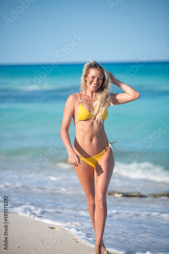 Young blonde woman in a yellow bikini running on the beach enjoying the sun smiling