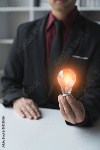 A young businessman in a smart suit holding a bright light bulb to express creative thinking New ideas with innovation and inspiration in online business.