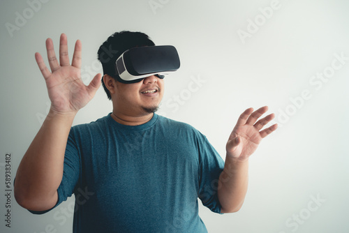 Asian man enjoy using VR headset for virtual reality access to online data network with laptop.