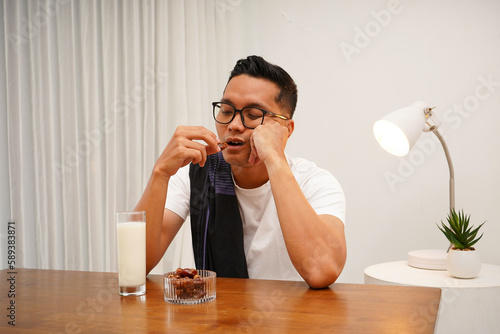 Photo of tired Asian Muslim man waking up early to have a morning breakfast on fasting month. Sahur concept in ramadan
