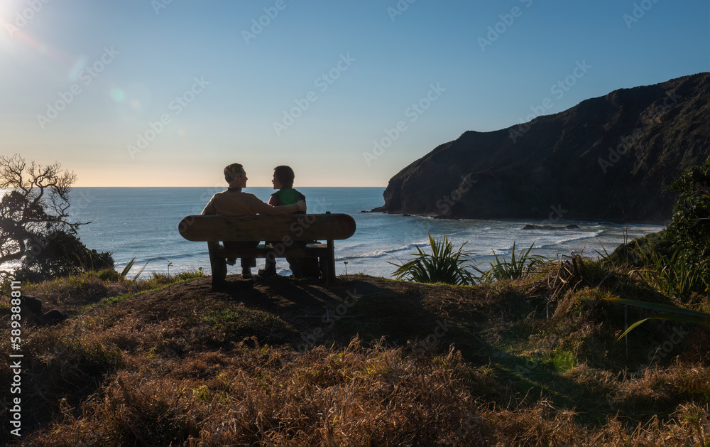 Couple looking at each other, sitting on the bench at Bethells Beach. Couple in love concept. Waitakere. Auckland.