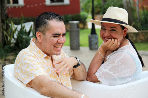 Latino couple of man and woman sitting on a bench in the form of confidant chairs in the city of Merida in Yucatan Mexico show their love with flirtatious looks and kisses