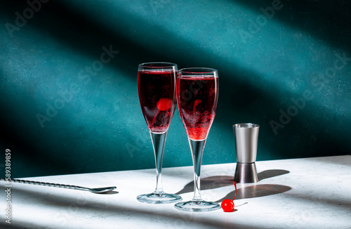 Kir Royale cocktail with black currant liqueur, prosecco wine and red cocktail cherry. Dark green background, hard light and shadow pattern