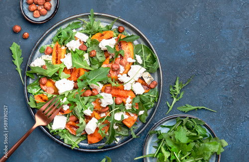 Grilled peach salad with feta cheese, hazelnuts and arugula on blue background, top view, copy space