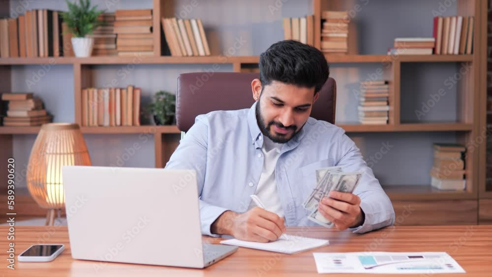 Successful indian business man counting money at workplace. Portrait of joyful businessman making notes using laptop having big income. Smiling man enjoy good deal at modern office. Made easy money. Successful indian business man counting money at workplace. Portrait of joyful businessman making notes using laptop having big income. Smiling man enjoy good deal at modern office. Made easy money.