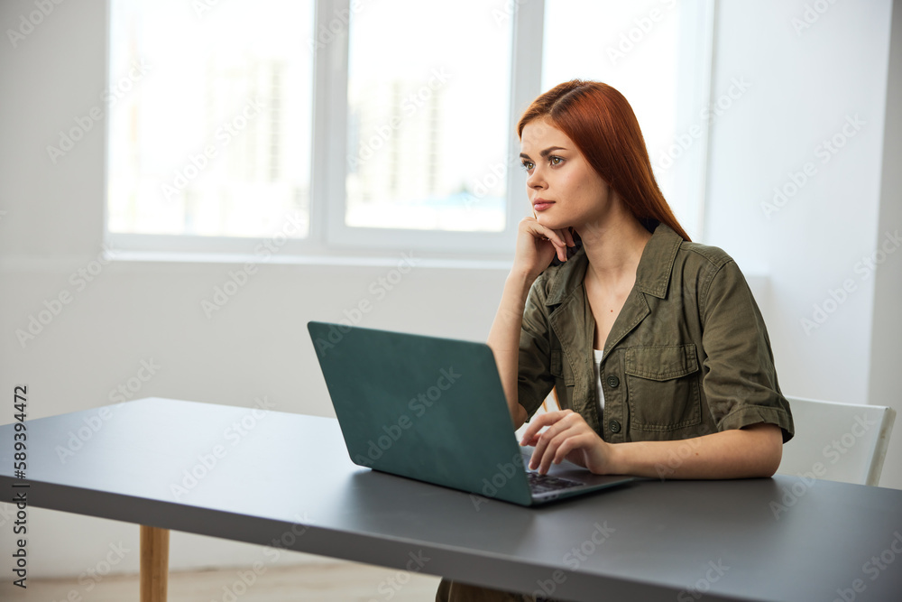 red-haired woman smiling thoughtfully sitting at work at a laptop red-haired woman smiling thoughtfully sitting at work at a laptop