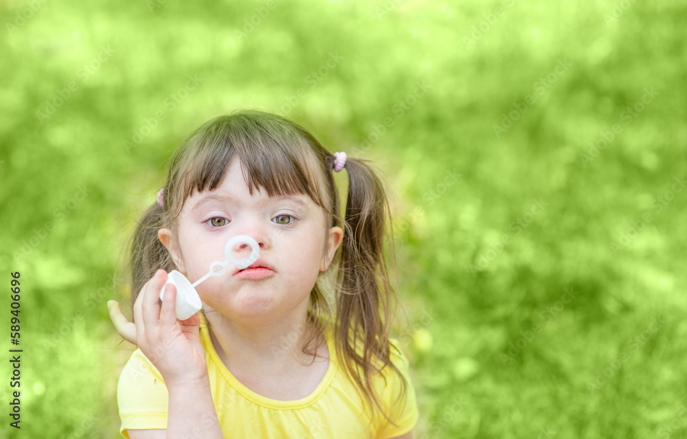 Little girl with syndrome down blows bubbles at summer park Little girl with syndrome down blows bubbles at summer park