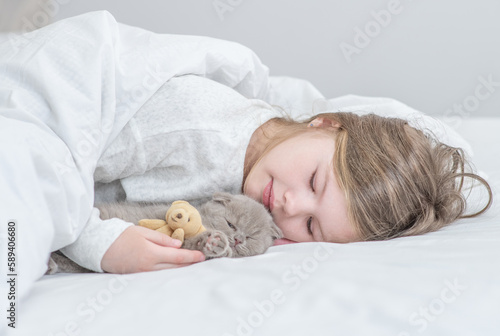 Happy little girl lying with tiny kitten on the bed at home
