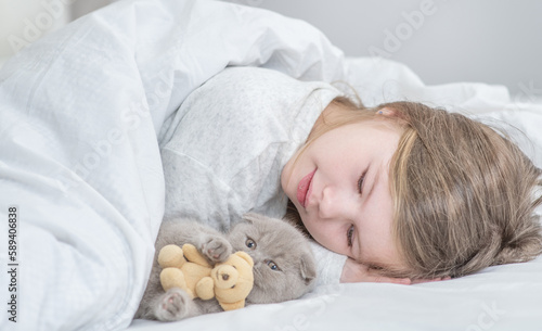 Happy little girl plays with tiny kitten on the bed at home