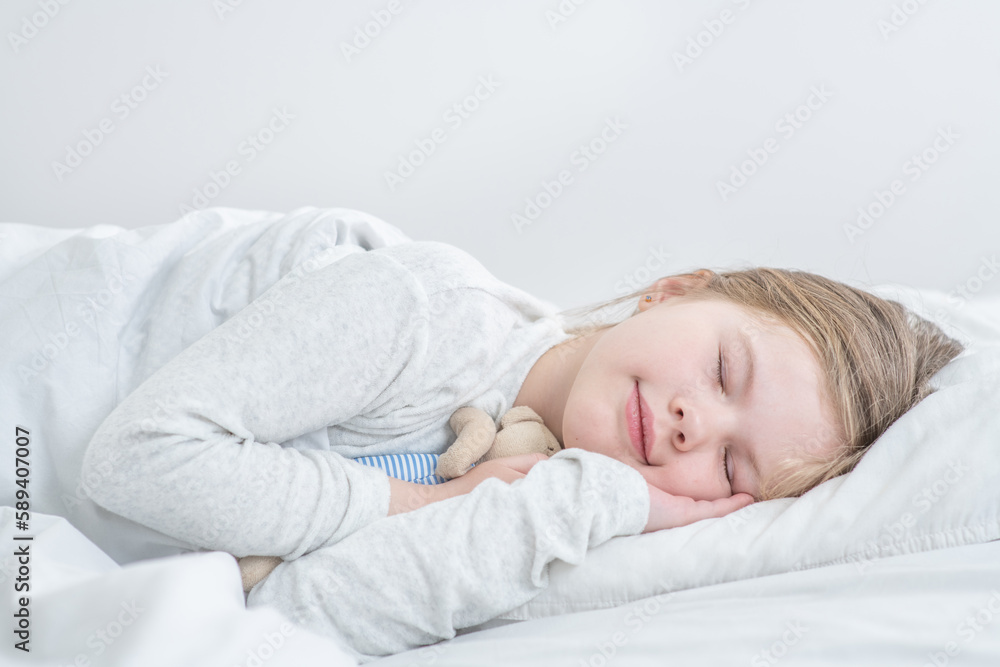Smiling little girl sleeps with toy bear on the bed at home Smiling little girl sleeps with toy bear on the bed at home
