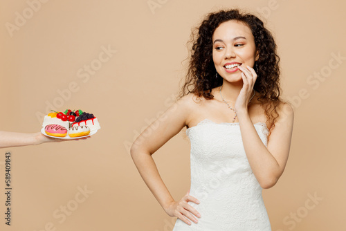 Minded fun beautiful young woman bride wearing wedding dress posing looking at cake with temtation isolated on plain pastel light beige background studio portrait. Ceremony celebration party concept. photo