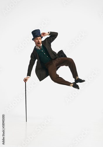 Portrait of a gentleman wearing old clothes and black cylinder jumping with cane up over white studio background. Levitating man