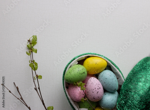  a green Easter egg filled with chocolate-filled eggs in colorful paper and next to it there are a couple of birch twigs with freshly shed leaves