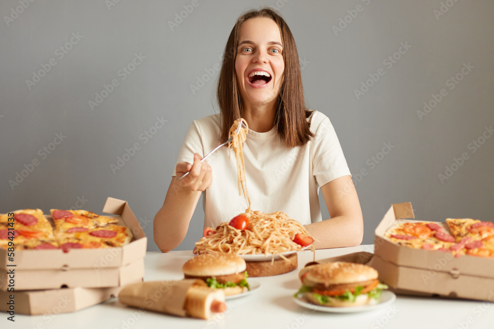 woman with brown hair wearing white T-shirt sitting at table isolated over gray background