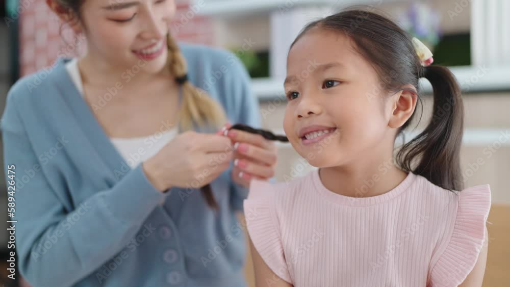 Happy loving family Asian mother is braiding hair her daughter's sitting on sofa at living room. Anti lice treatment Happy loving family Asian mother is braiding hair her daughter's sitting on sofa at living room. Anti lice treatment