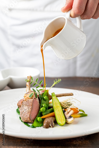 Foto Chef pouring sauce on lamb chops with various vegetables at a fine dining restau