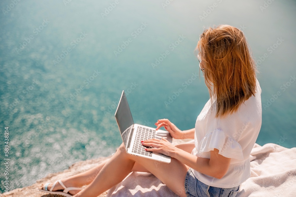 Freelance women sea working on the computer. Good looking middle aged woman typing on a laptop keyboard outdoors with a beautiful sea view. The concept of remote work.