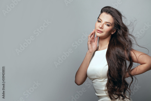 Pretty young adult woman with long curly dark healthy hair against gray studio wall banner background