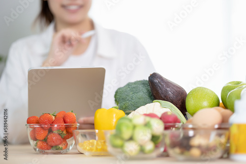 Close up hand of professional nutrition healthful surrounded by a variety of fresh fruits and vegetables working on digital tablet. Concept of right nutrition, diet and healthcare.