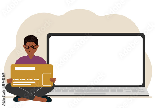 A man sits cross-legged and holds a large plastic card. Next to the man is a large laptop with space for text.