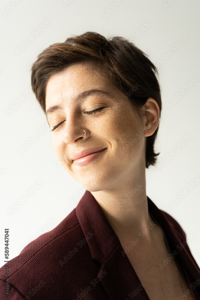 portrait of happy young woman with short brunette hair smiling with closed eyes isolated on grey. portrait of happy young woman with short brunette hair smiling with closed eyes isolated on grey.