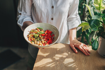 Young woman eating healthy food sitting in the beautiful interior with green flowers on the background