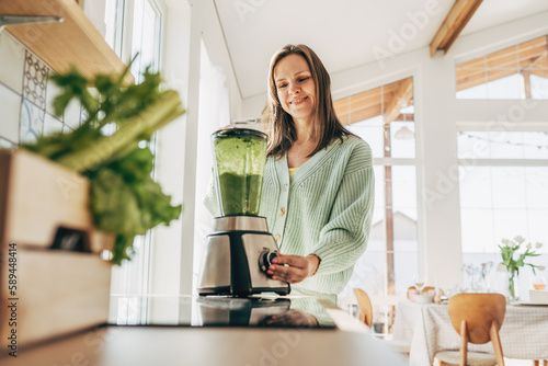 Woman preparing tasty green smoothie in kitchen