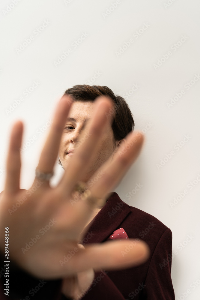 Fototapeta premium smiling woman in trendy blazer looking at camera through outstretched hand on grey background.