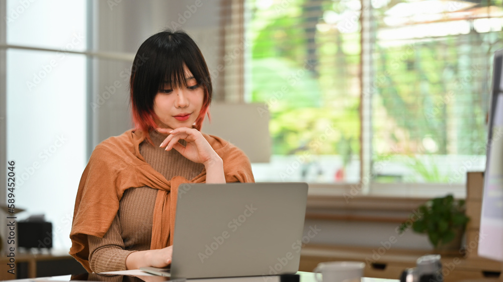 Portrait of young stylish woman using laptop at home office. Freelance, creative occupation, e-learning concept Portrait of young stylish woman using laptop at home office. Freelance, creative occupation, e-learning concept