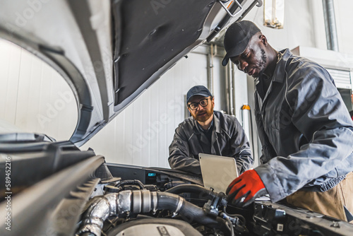 medium shot of two mechanics using a laptop near car engine compartment, car repair shop. High quality photo
