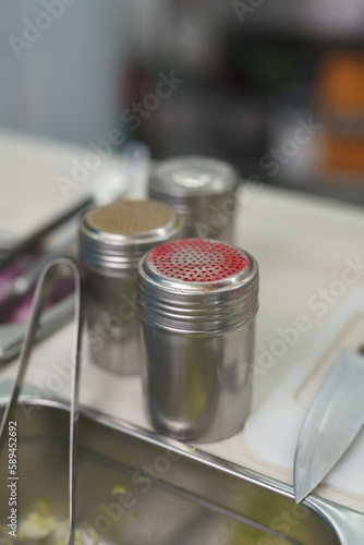 Containers with paprika powder, pepper and salt on a commercial kitchen counter in a restaurant photo