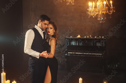 Papier peint sexy couple blonde woman holding hand of handsome man slow dance in dark gothic room piano candles are burning, candlelight holiday party