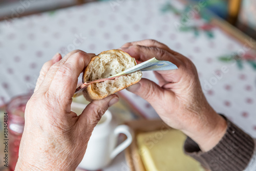 Alte Frau Oma Rentnerin sitzt am gedeckten Frühstückstisch beim Frühstück und isst ein mit Euro Geldscheinen belegtes Brötchen , Deutschland